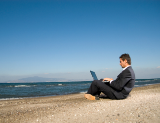 Man dressed in suit, using laptop while sitting on beach